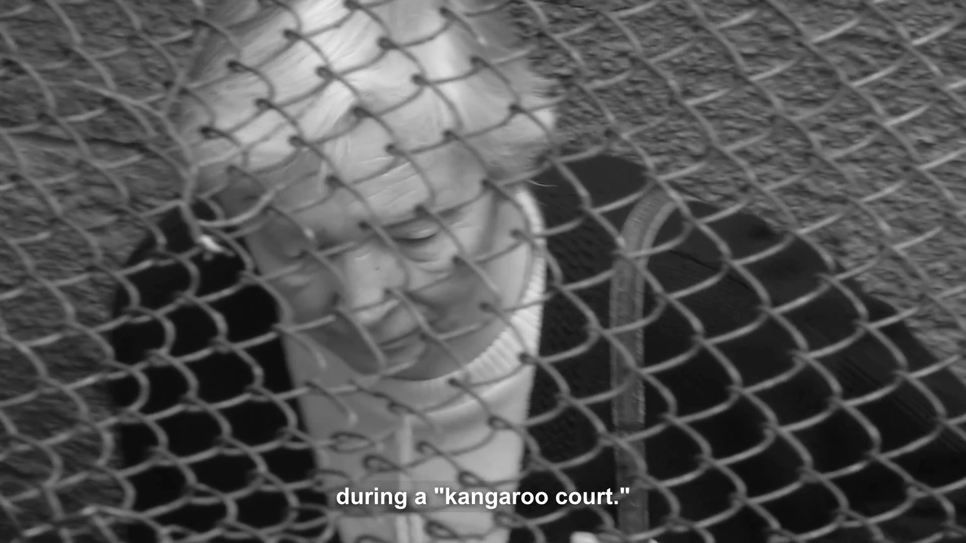 A woman seen through a wire fence in MONUMENT, with the film’s English subtitle.