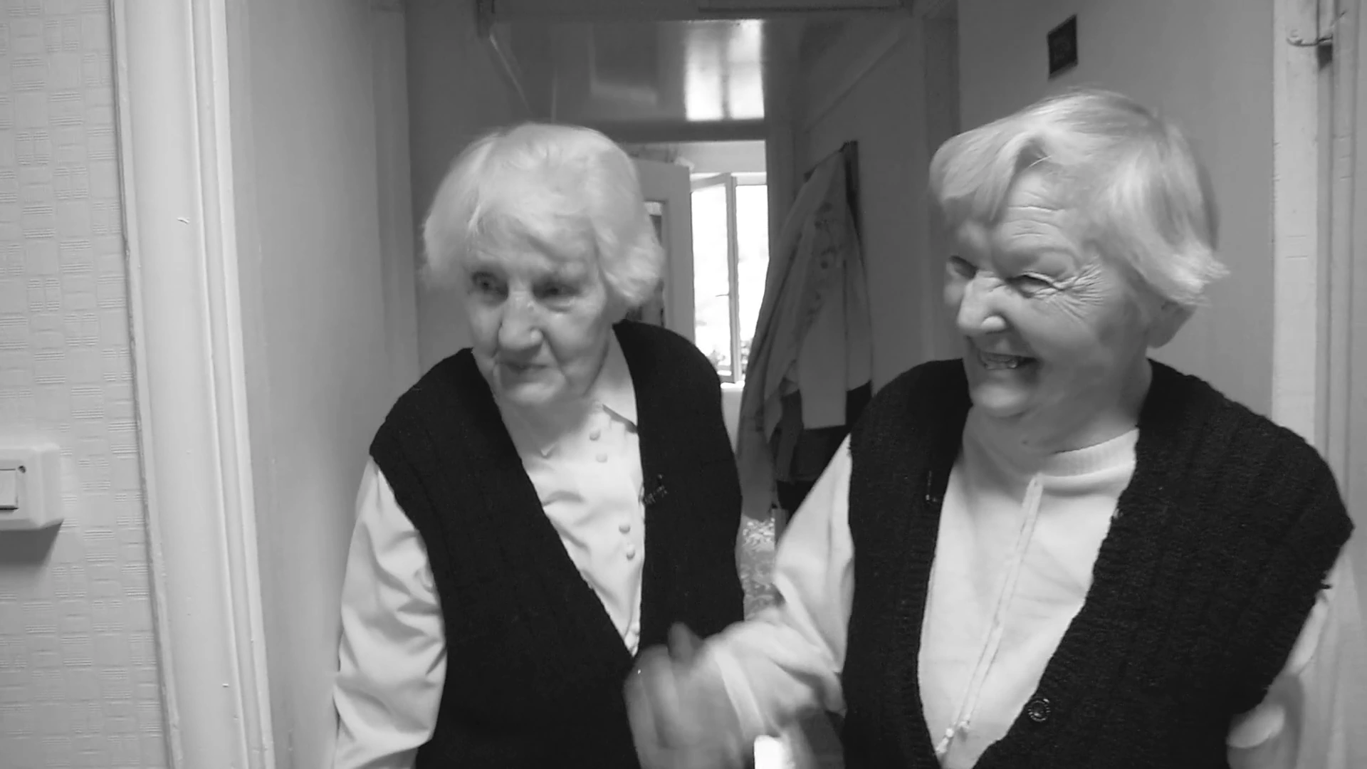 Two women smiling together in a doorway in MONUMENT.